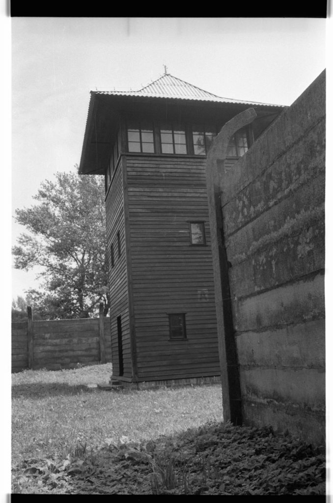 B/W photo of concrete and wood siding buildings. An faded "A" is painted on the side of the wooden building. Nikon D70 Film Camera 2004 - Negative Scan from Nikon COOLSCAN V ED 2008