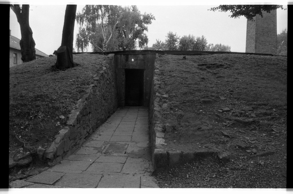 B/W photo of rear entrance to crematorium. Floors and buildings are all brick with a smoke stack. Nikon D70 Film Camera 2004 - Negative Scan from Nikon COOLSCAN V ED 2008