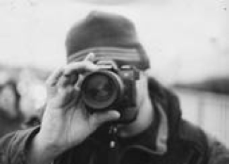 B/W picture of me focusing lens on a camera. My face is obtused and I am wearing a winter hat. Circa 2000's